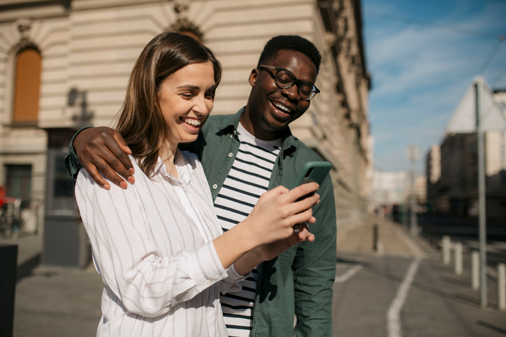 Happy diverse couple laughing at something on a cell phone. 