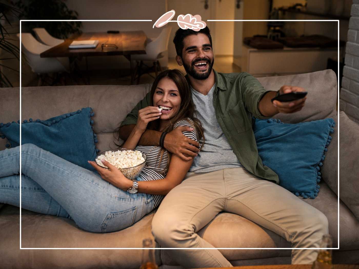 A happy couple cuddling on a couch, enjoying popcorn while watching TV - Fabulous Flowers and Gifts.