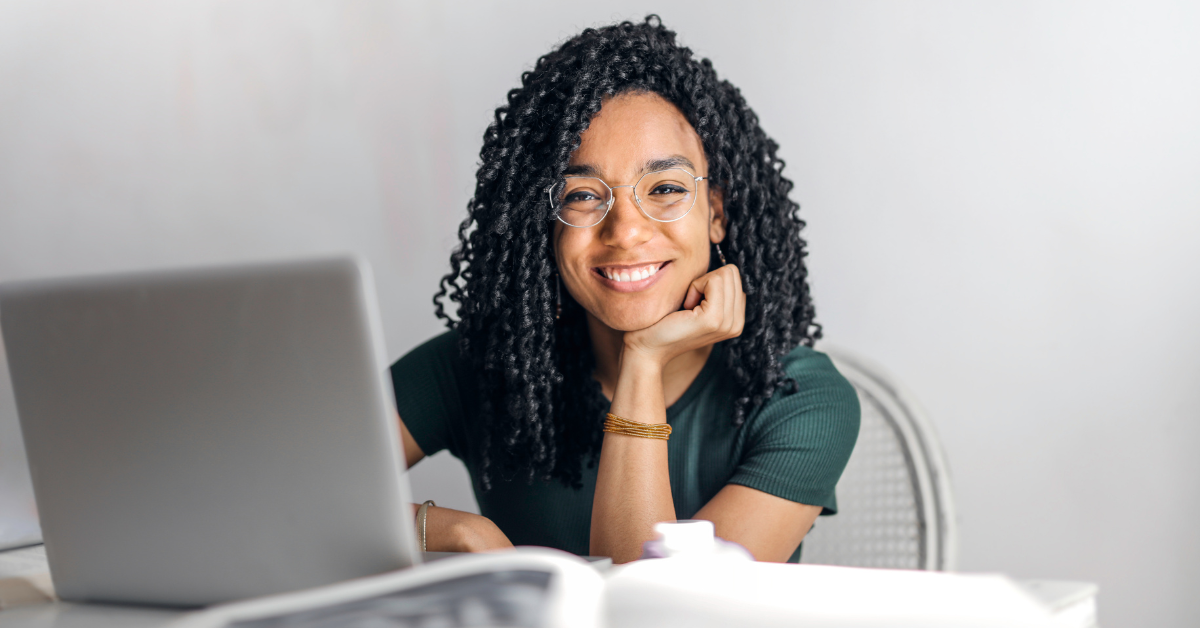 A smiling woman with glasses working on her laptop; learning about tax and compliance for freelancers.