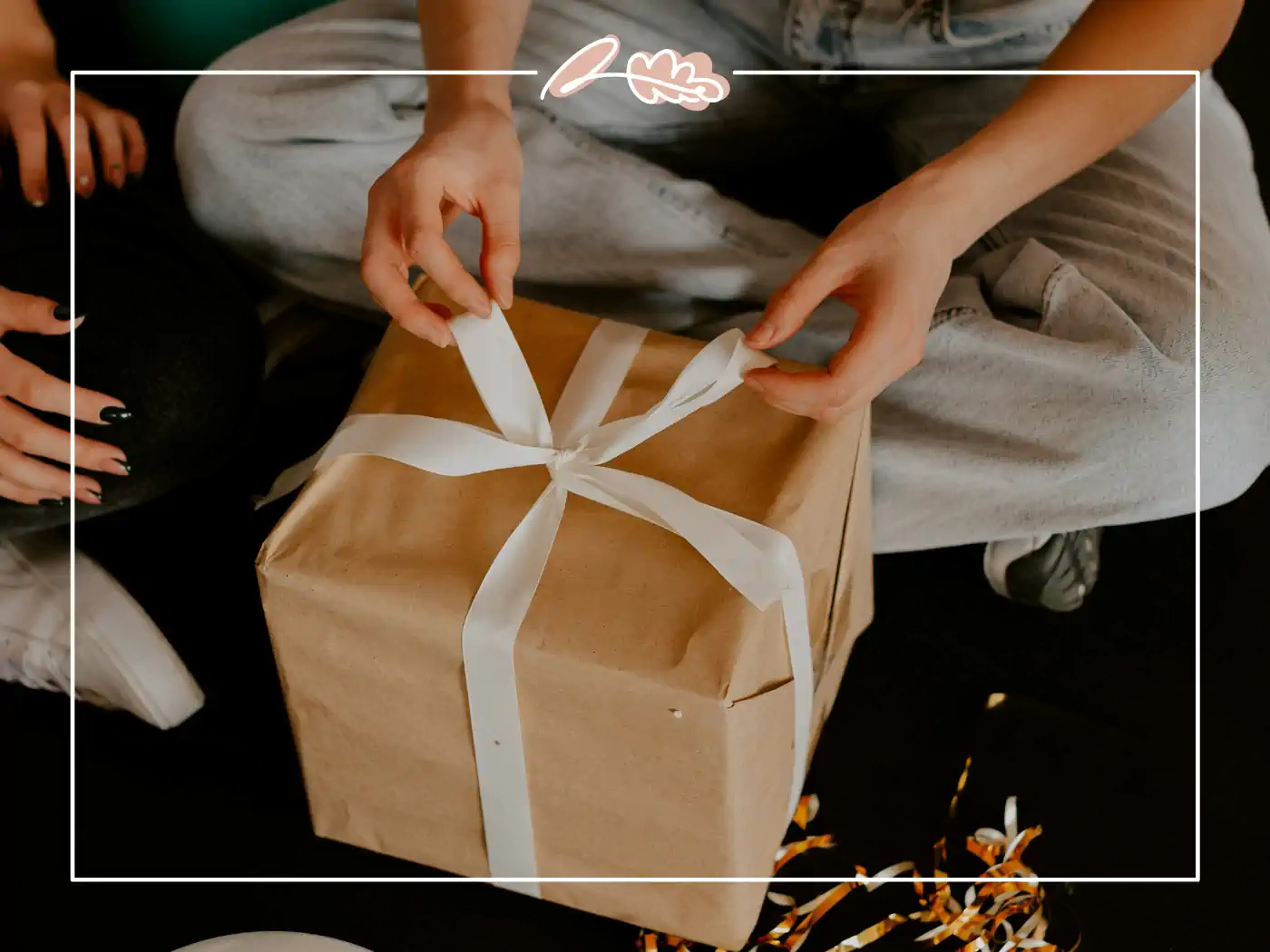 Close-up of hands unwrapping a brown paper gift box with a white ribbon. Fabulous Flowers and Gifts.