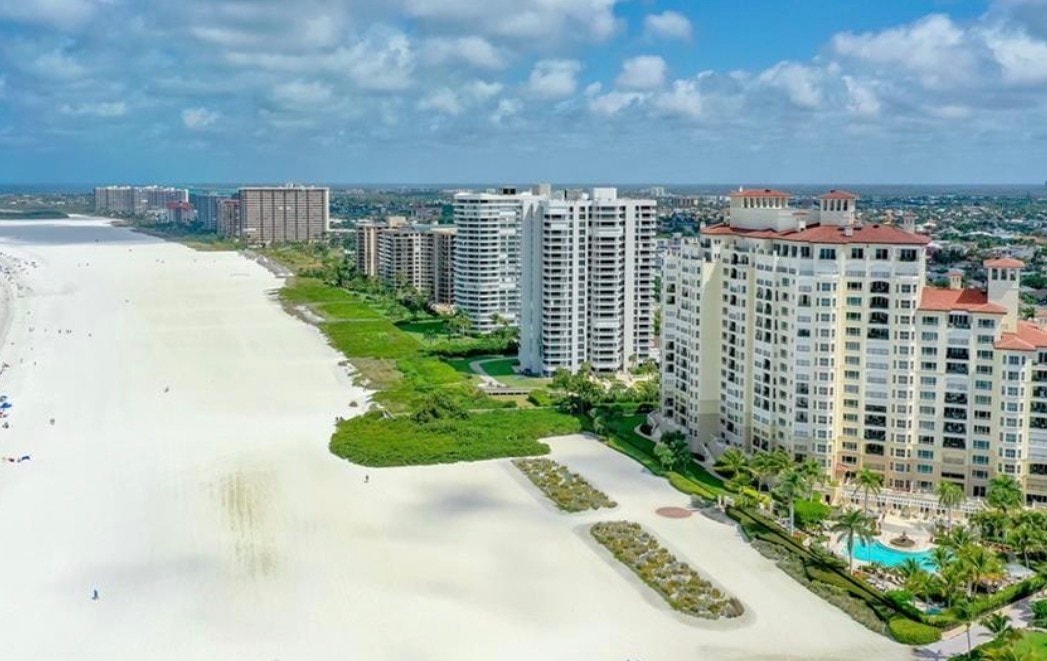 An aerial view of Collier Boulevard showcases luxury condominiums and beachfront properties along the picturesque coastline of Marco Island, highlighting the elegance of the area with its stunning views of the Gulf. The image captures the vibrant community, featuring amenities like pools and proximity to local restaurants and golf courses, perfect for residents and guests alike.