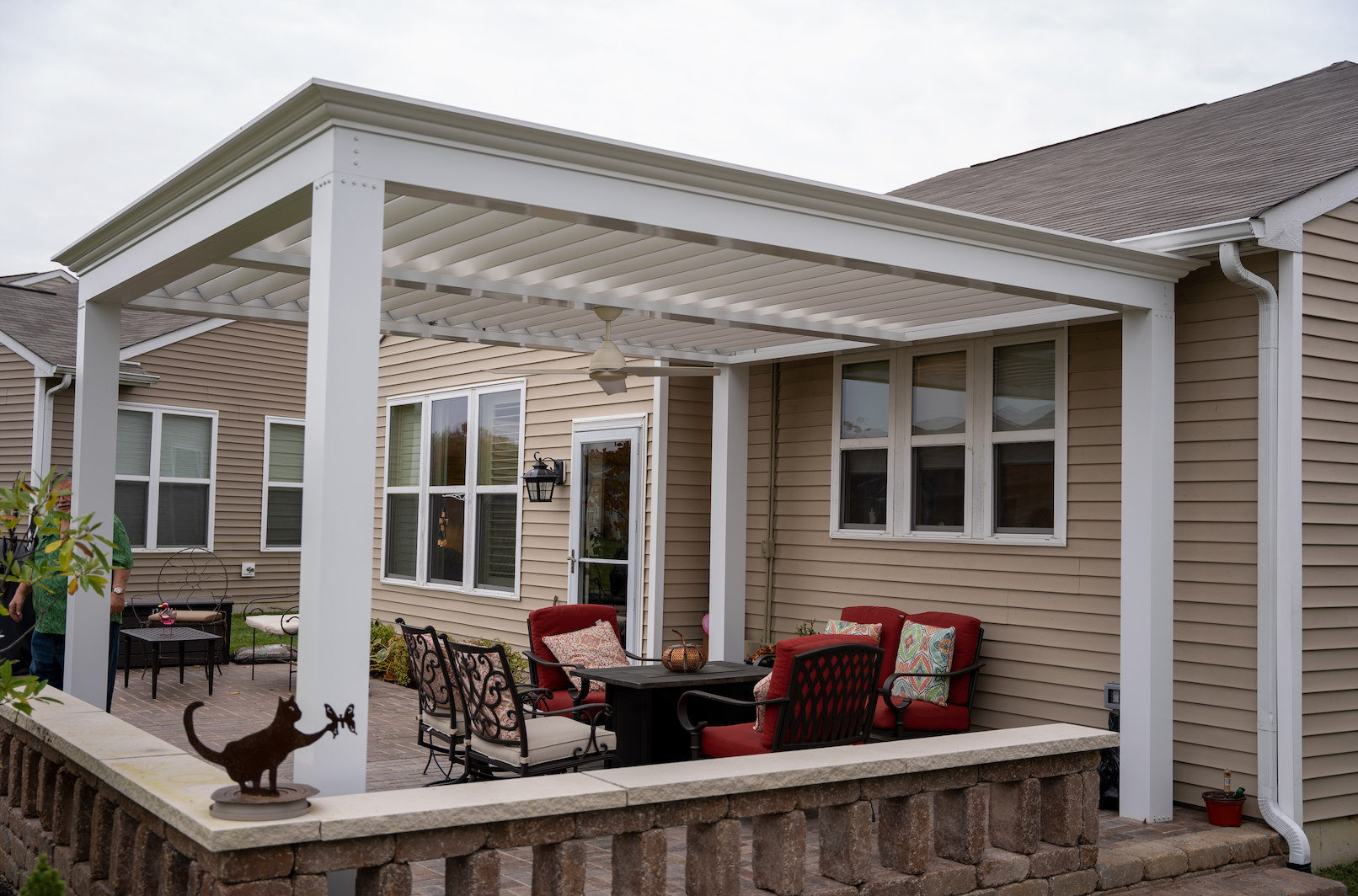 A white aluminum louvered pergola on a stone back porch