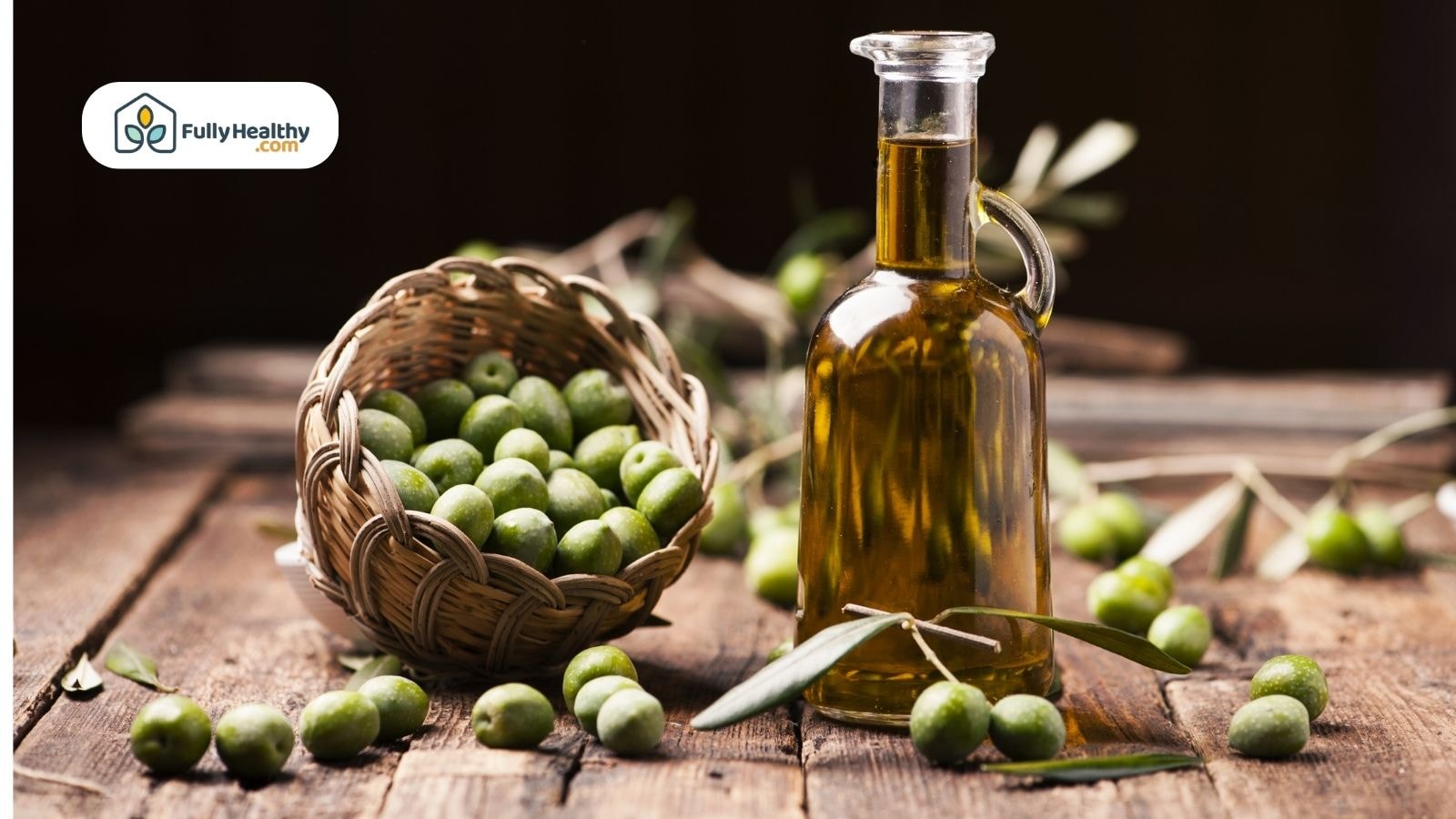 Glass bottle of olive oil beside fresh green olives in basket