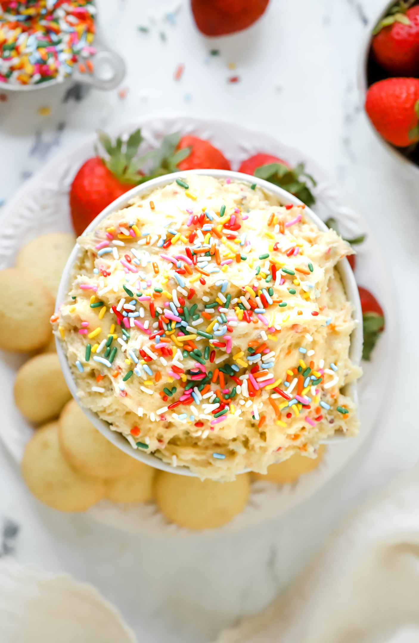 top down view of a bowl of cake batter dip on a plate surrounded by strawberries and nilla wafers