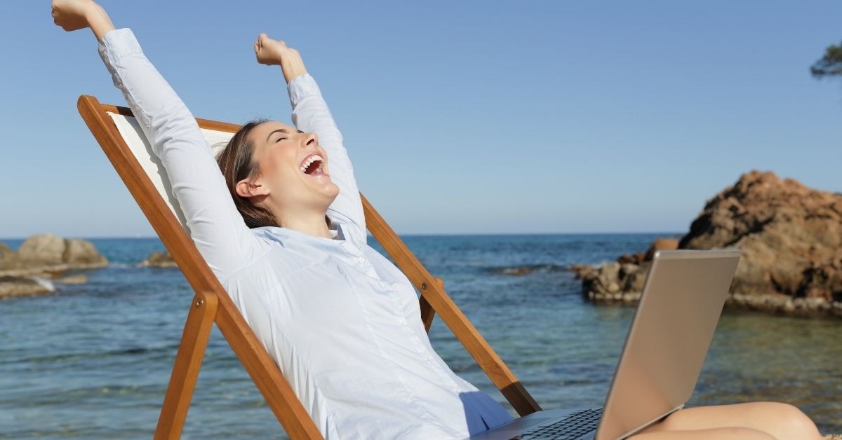 A woman celebrating while working on her laptop by the beach, possibly after resolving excess Social Security tax withheld issues.