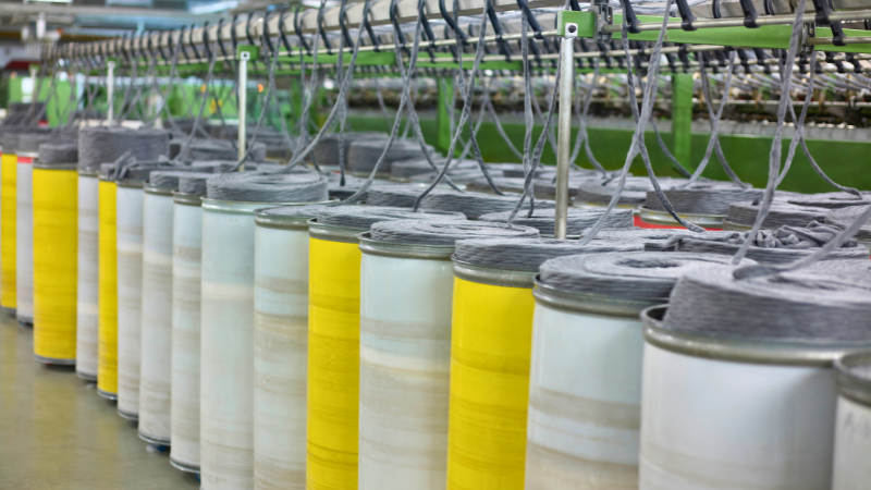 A row of yellow and white polyester spools of thread are being processed by machinery in a factory setting.