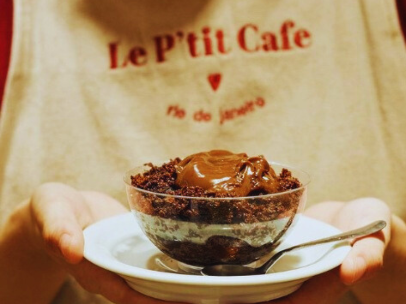 Pessoa com avental do P'etit Cafe segura um prato com sobremesa de chocolate. Imagem: Reprodução Instagram.
