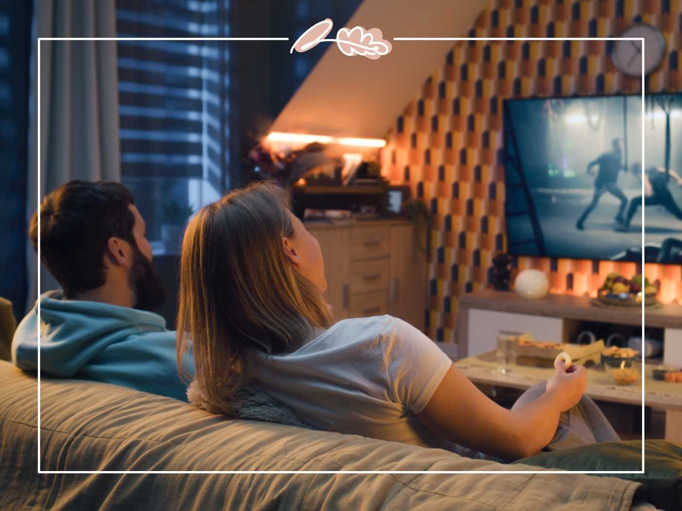 A couple relaxing on a couch, watching an action-packed movie on TV in a dimly lit, stylish living room - Fabulous Flowers and Gifts.