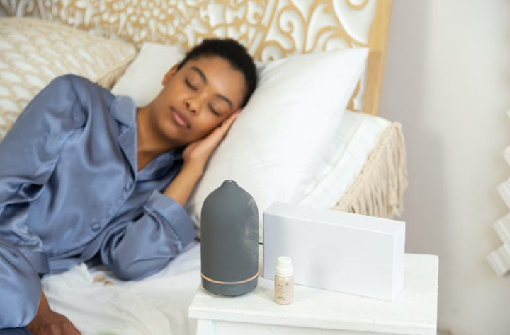 Woman sleeping in pajamas in a nice bed with a defuser on the nightstand