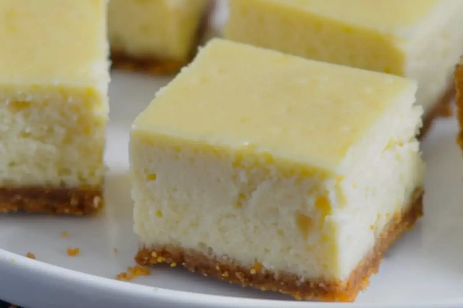 A close-up of creamy cheesecake squares on a plate, featuring a golden crust.