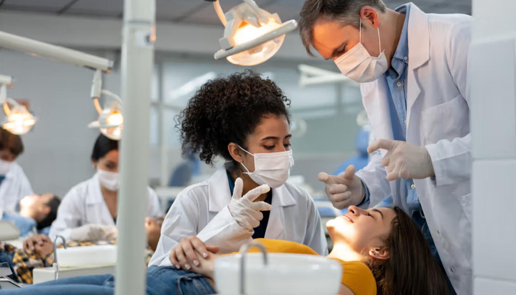 Tannlegestudenter får veiledning fra lærer mens de øver på pasientbehandling i en klinisk utdanningssituasjon med flere behandlingsstasjoner.