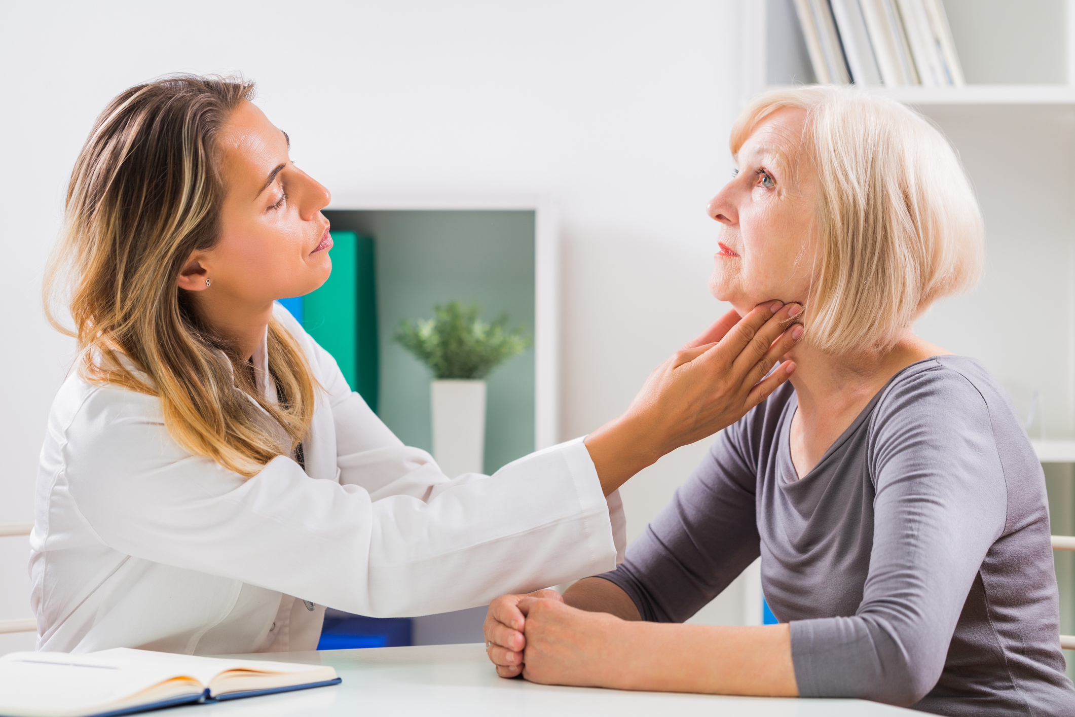 An image of a female doctor feeling her patient's throat.