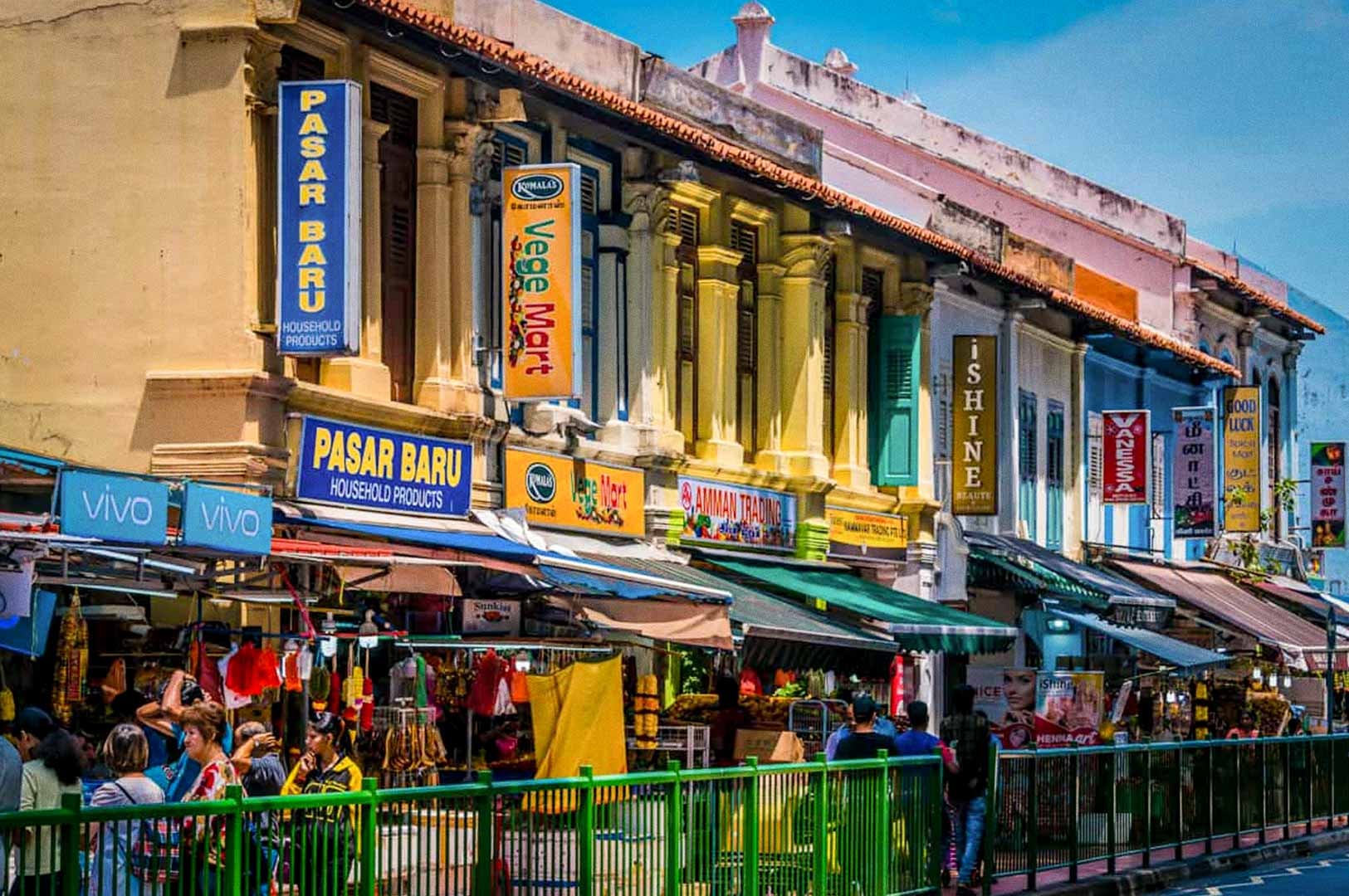 A jewelry shop display filled with gold necklaces, bangles, and rings arranged on red stands and trays behind a glass window in Little India.