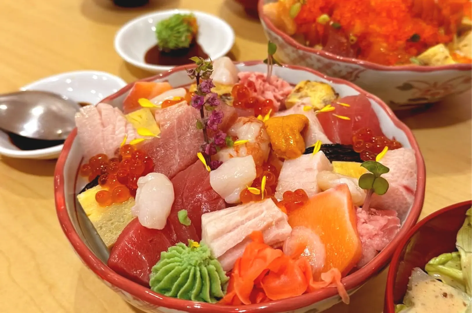 A close-up of a luxurious premium chirashi don bowl loaded with fresh uni, scallops, salmon roe, and assorted sashimi slices.
