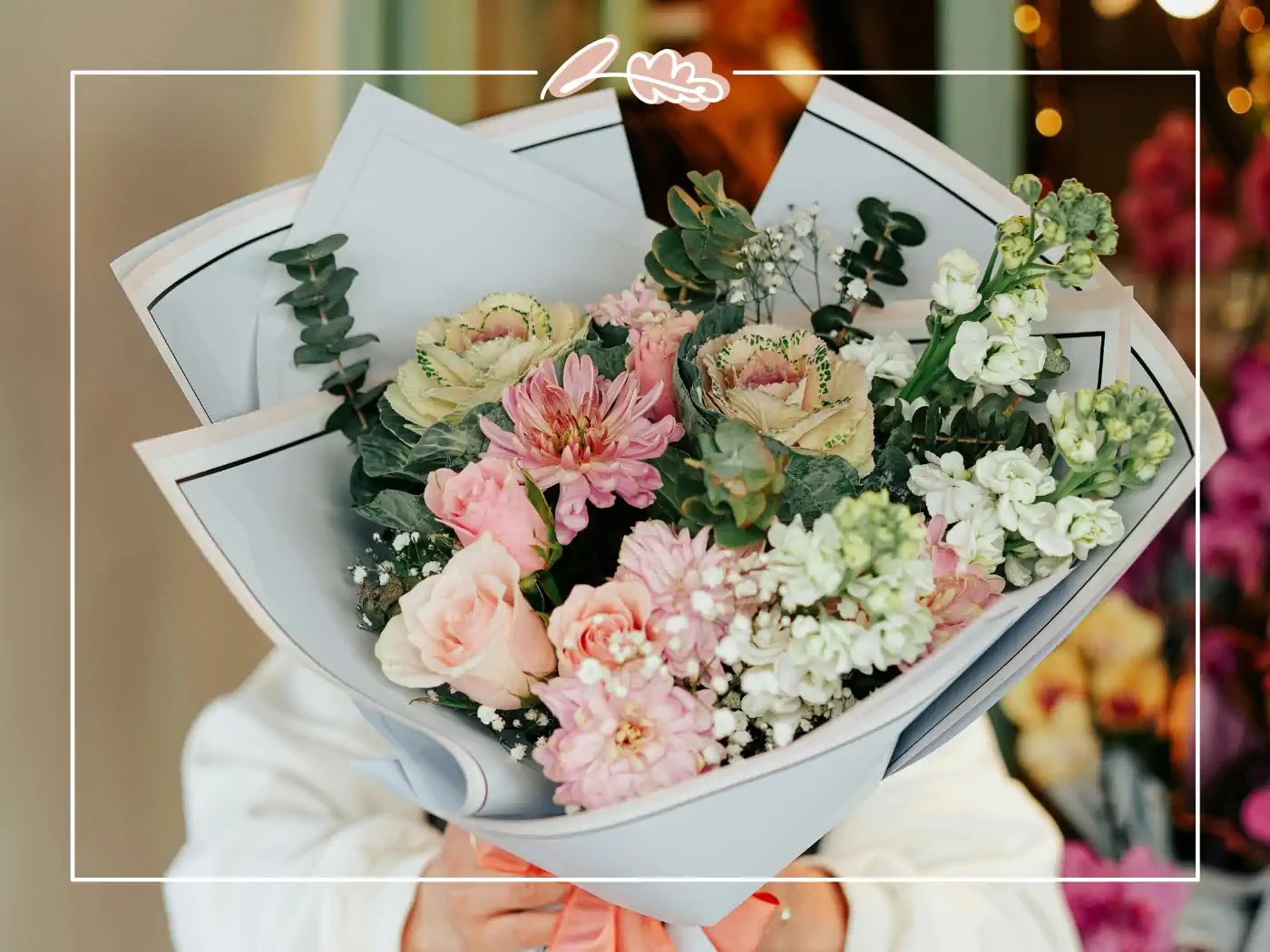 A close-up of a person holding a beautifully arranged bouquet of pastel-colored flowers wrapped in white paper.