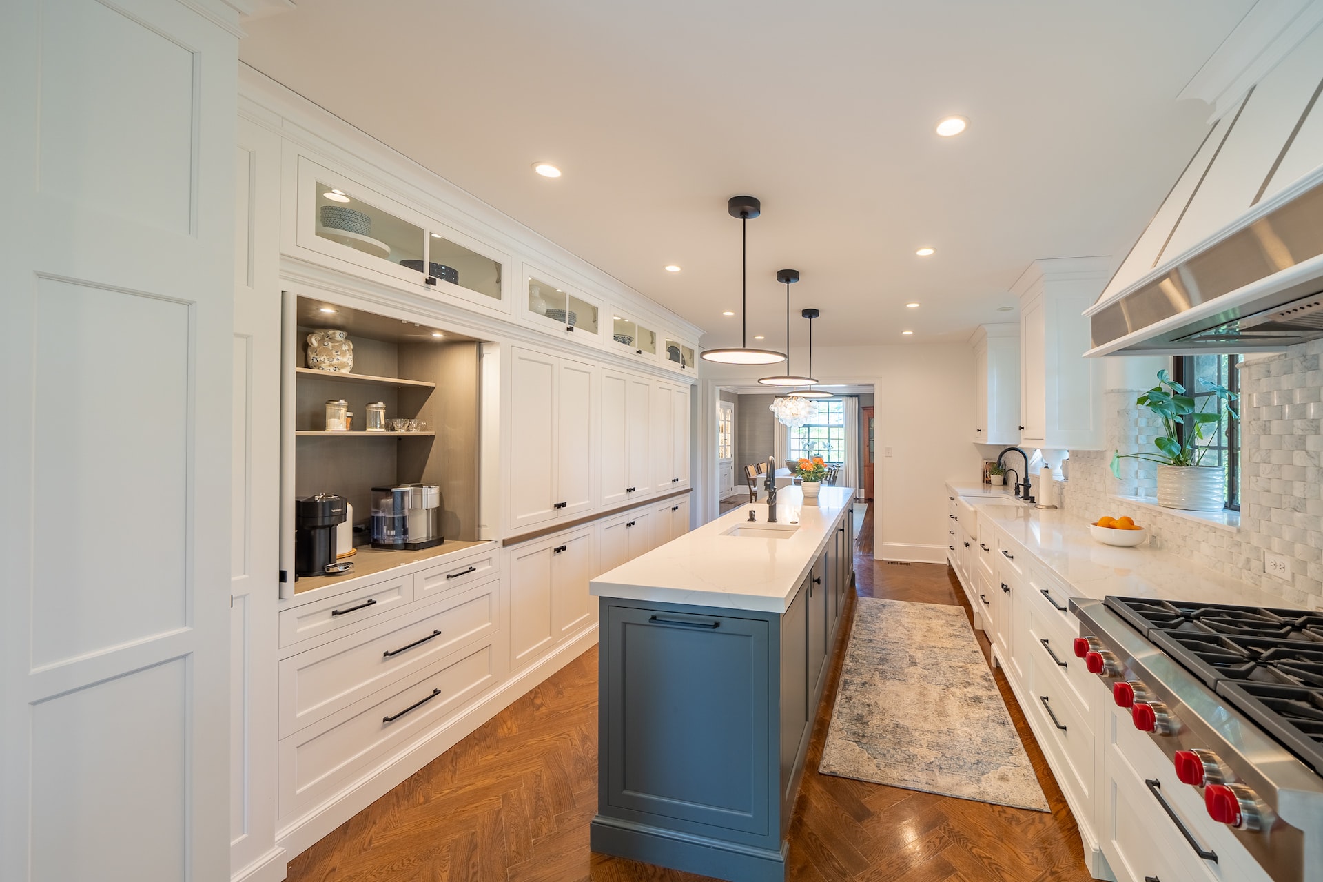 Photo of a mostly white kitchen. On the left, one cabinet section with bar doors is open to reveal a coffee maker and shelves with coffee-making accessories.
