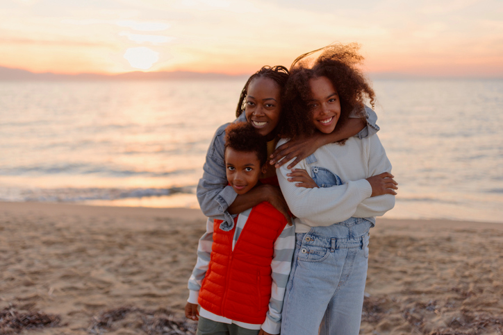 Beautiful mom hugging her two kids on the beach. 