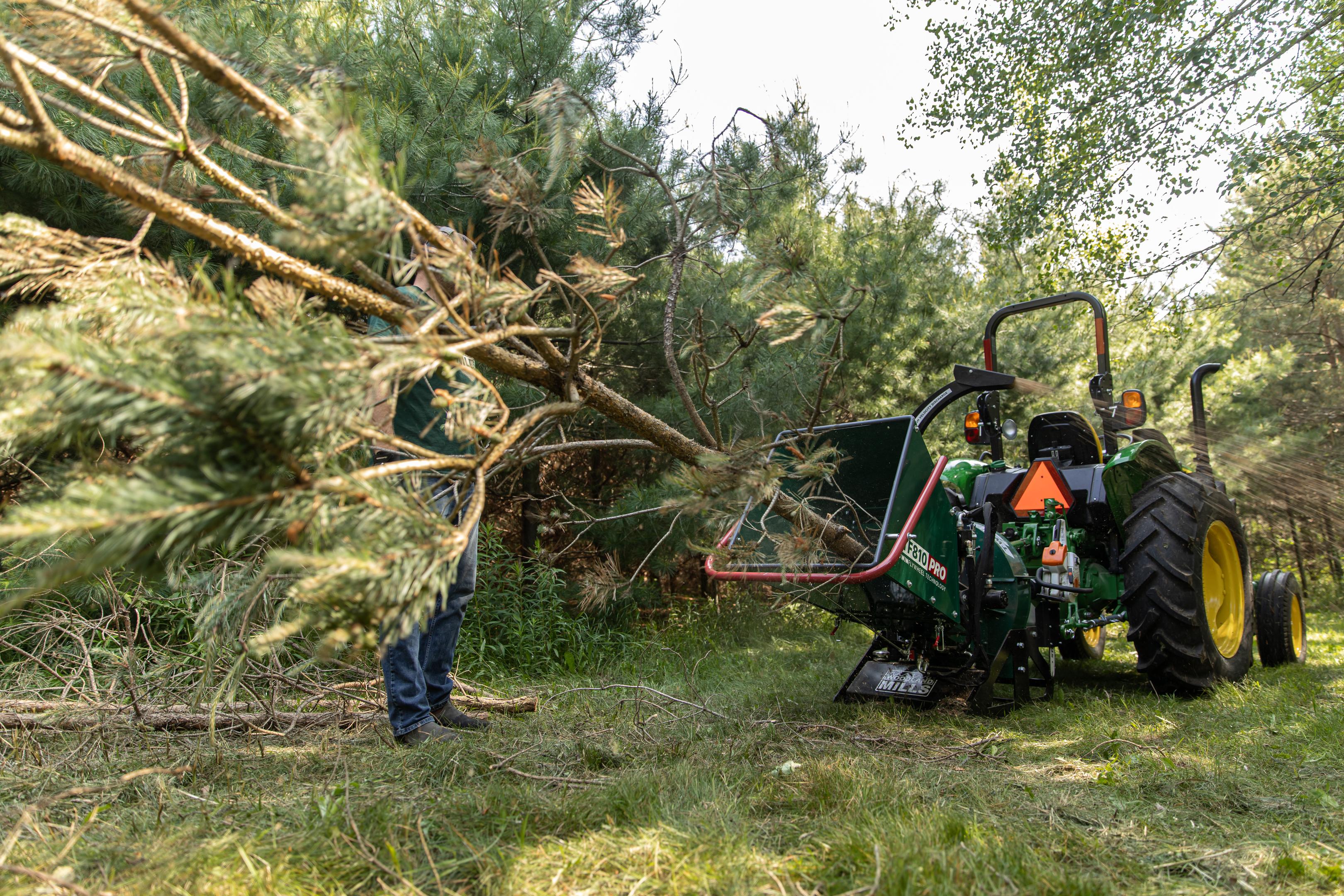 An entire tree being chipped by a Woodland Mills wood chipper attached to a tractor.