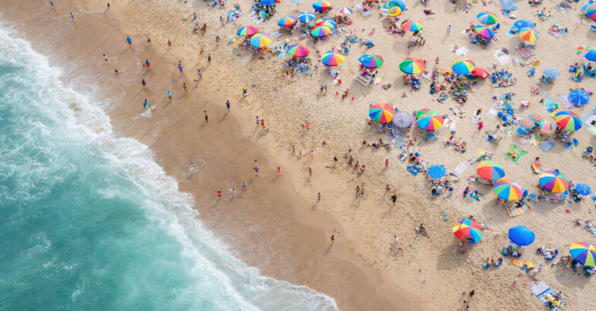 Aerial view of a busy Jersey Shore beach with colorful rainbow umbrellas and families enjoying a summer day along the Atlantic coastline.