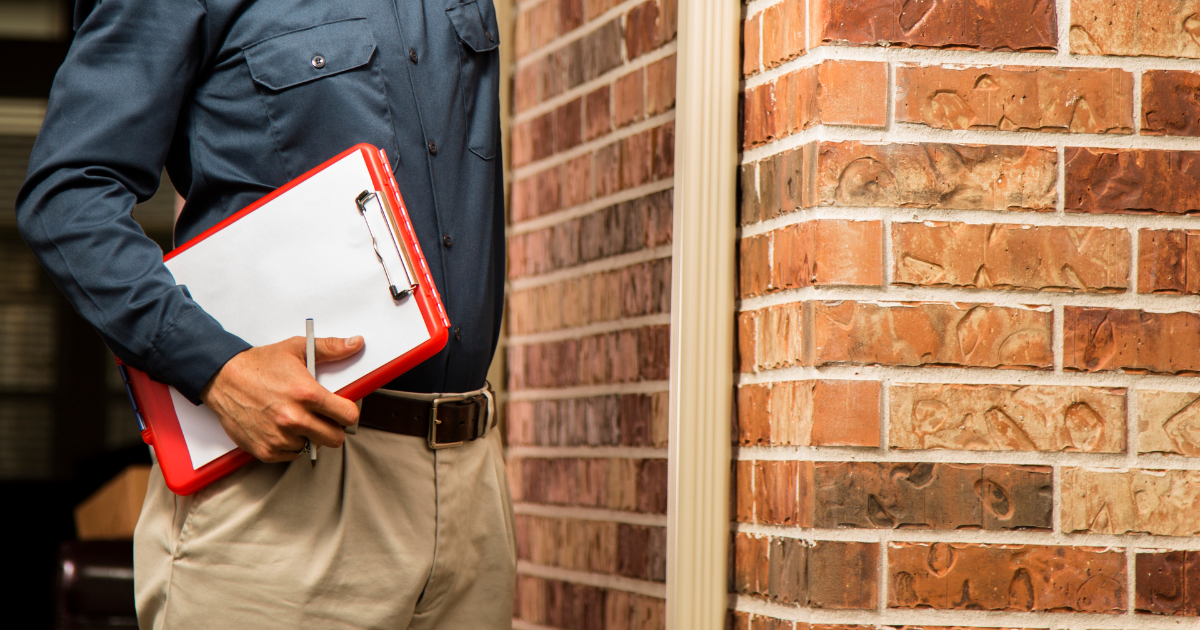 Home inspector holding a clipboard beside a brick exterior wall during a property inspection in Augusta, GA