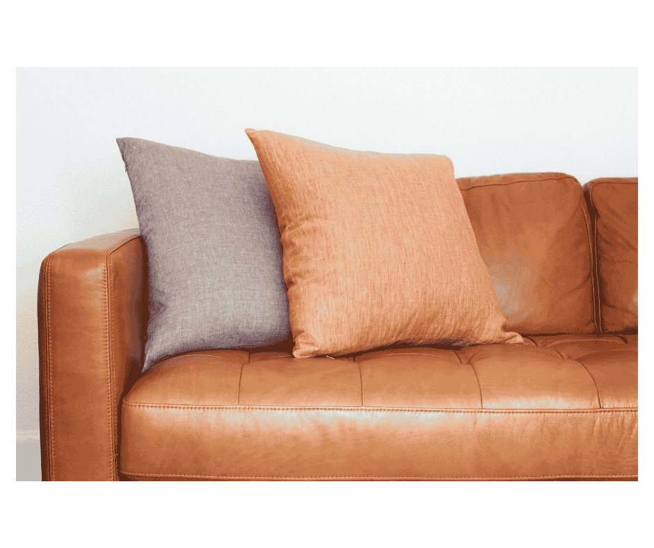 Clean brown leather sofa with decorative grey and peach cushions in a modern living room