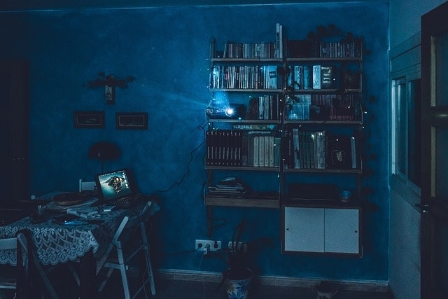 Dimly lit room with a desk, laptop, and bookshelf filled with books and decorations.