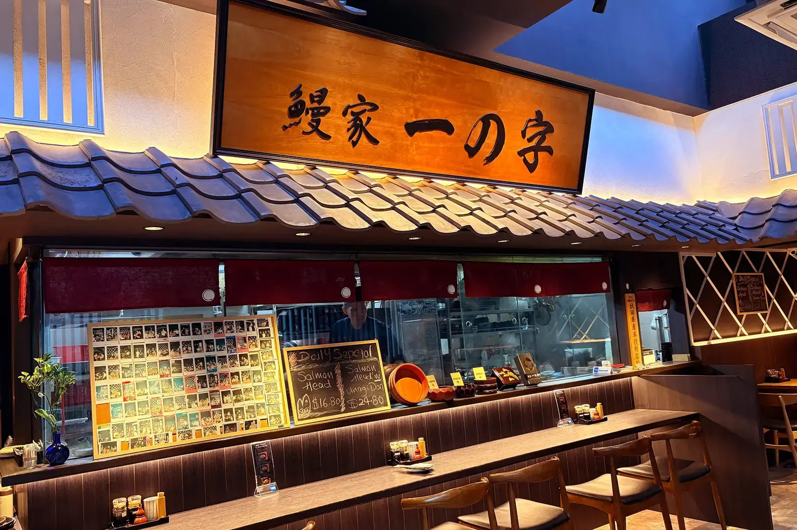 Unagiya Ichinoji interior featuring a tiled roof-style counter, Japanese signboard, menu displays, and wooden bar seating.