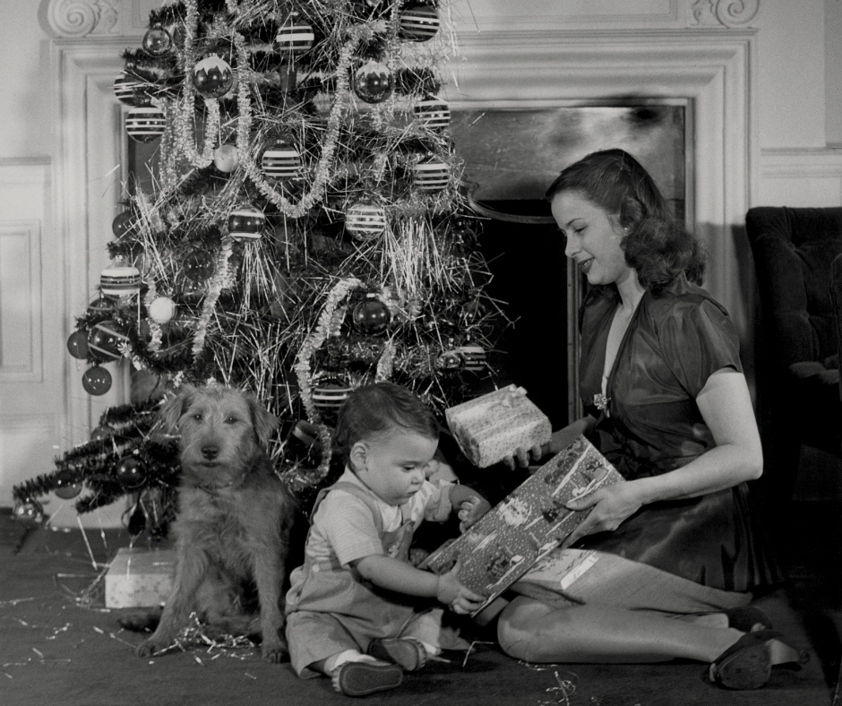 a child, mom, and dog sit in front of a christmas tree