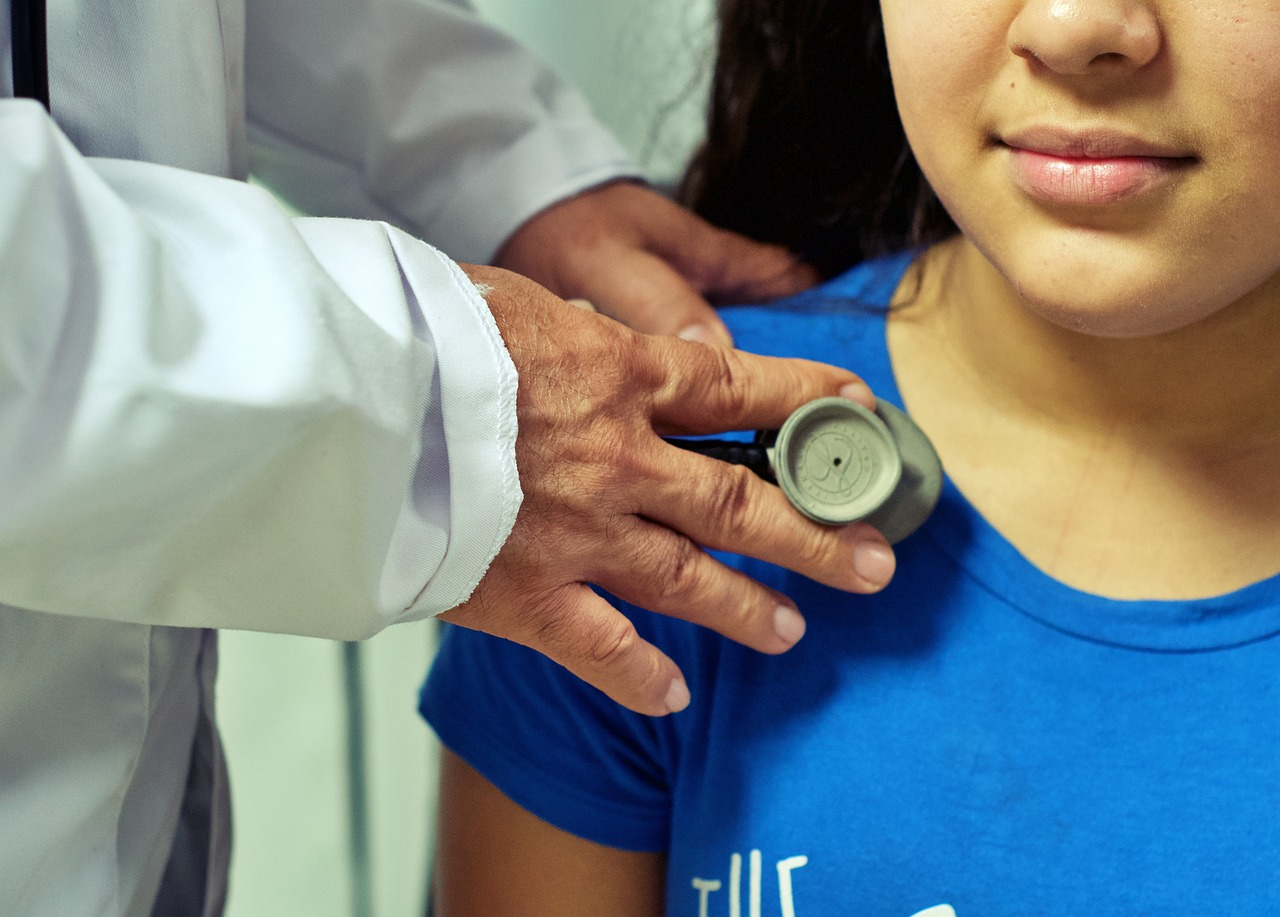 An image of a doctor listening to a girl's chest with a stethoscope. 