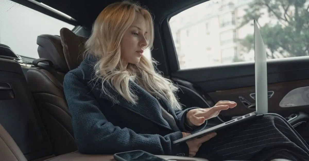 OnlyFans creator in a luxury car using her laptop for luxury tax planning and financial management.