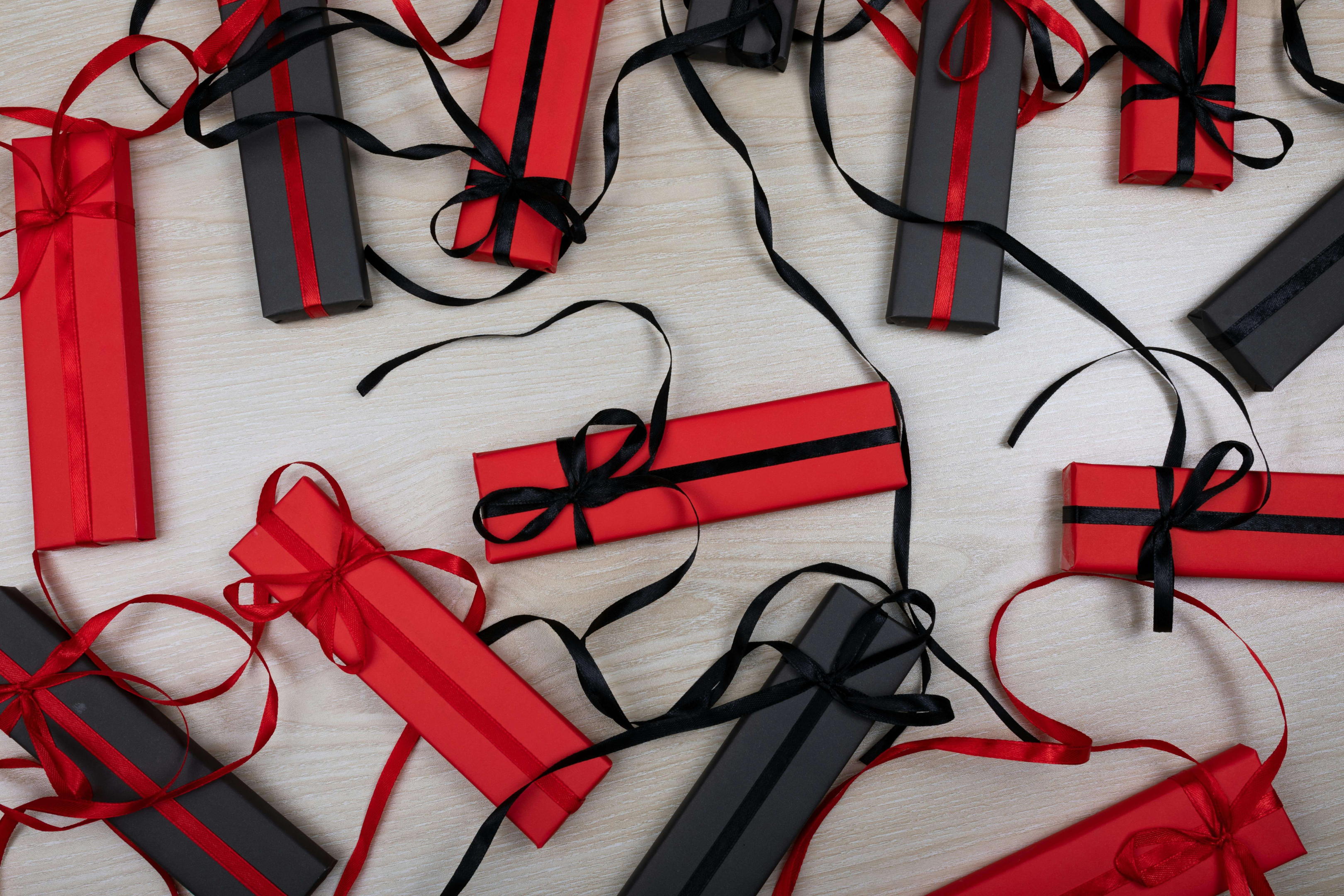 Assortment of red and black gift boxes with elegant ribbons on a wooden surface.