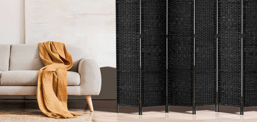 An Artiss black rattan room divider with six panels, next to a light grey sofa with an orange blanket.