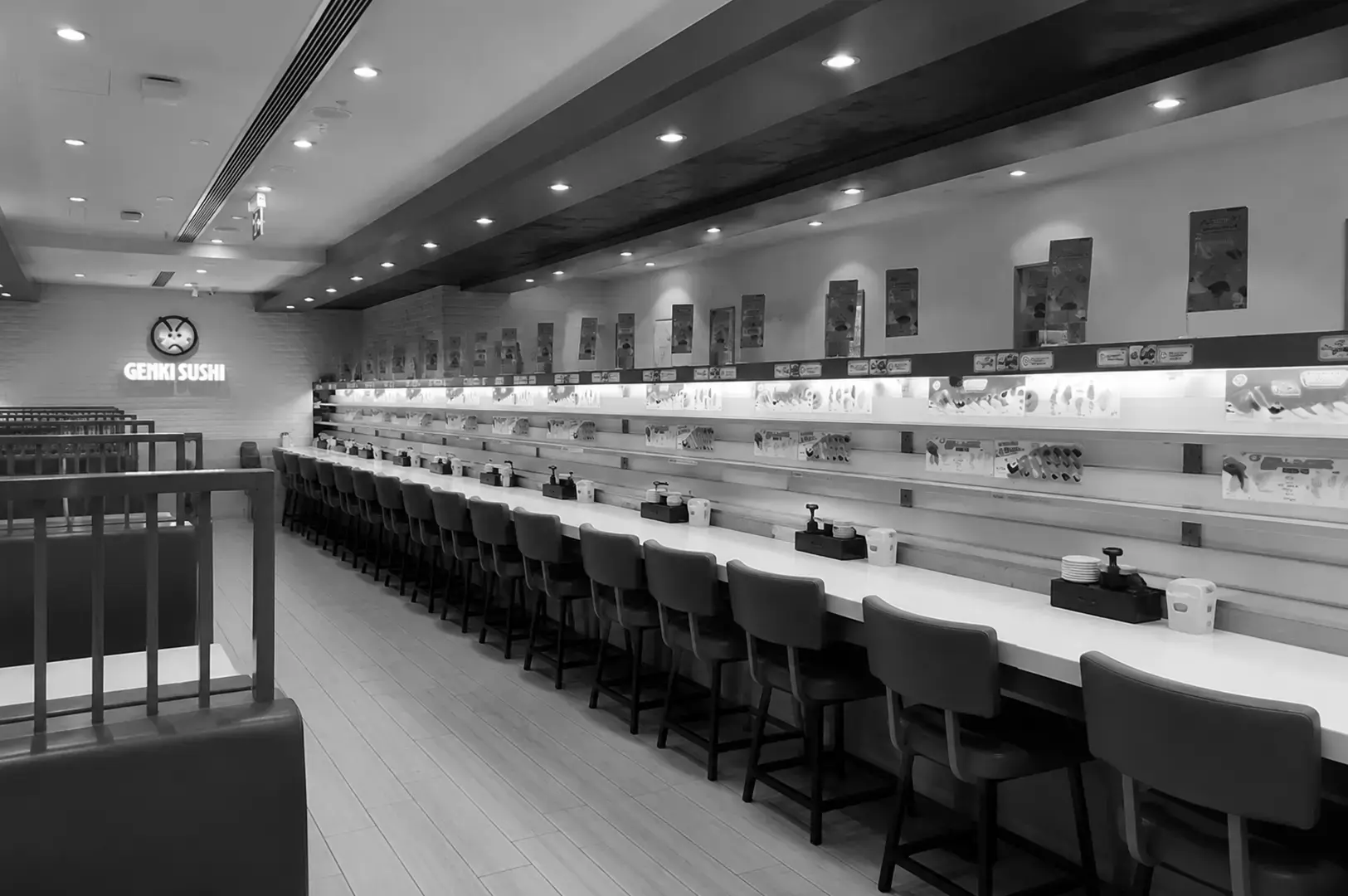 Spacious conveyor belt sushi restaurant with long counter seating and illuminated menu displays.