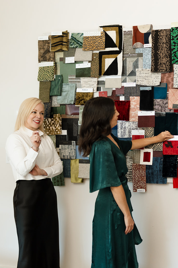 Two designers examining a wall of fabric samples in a studio.