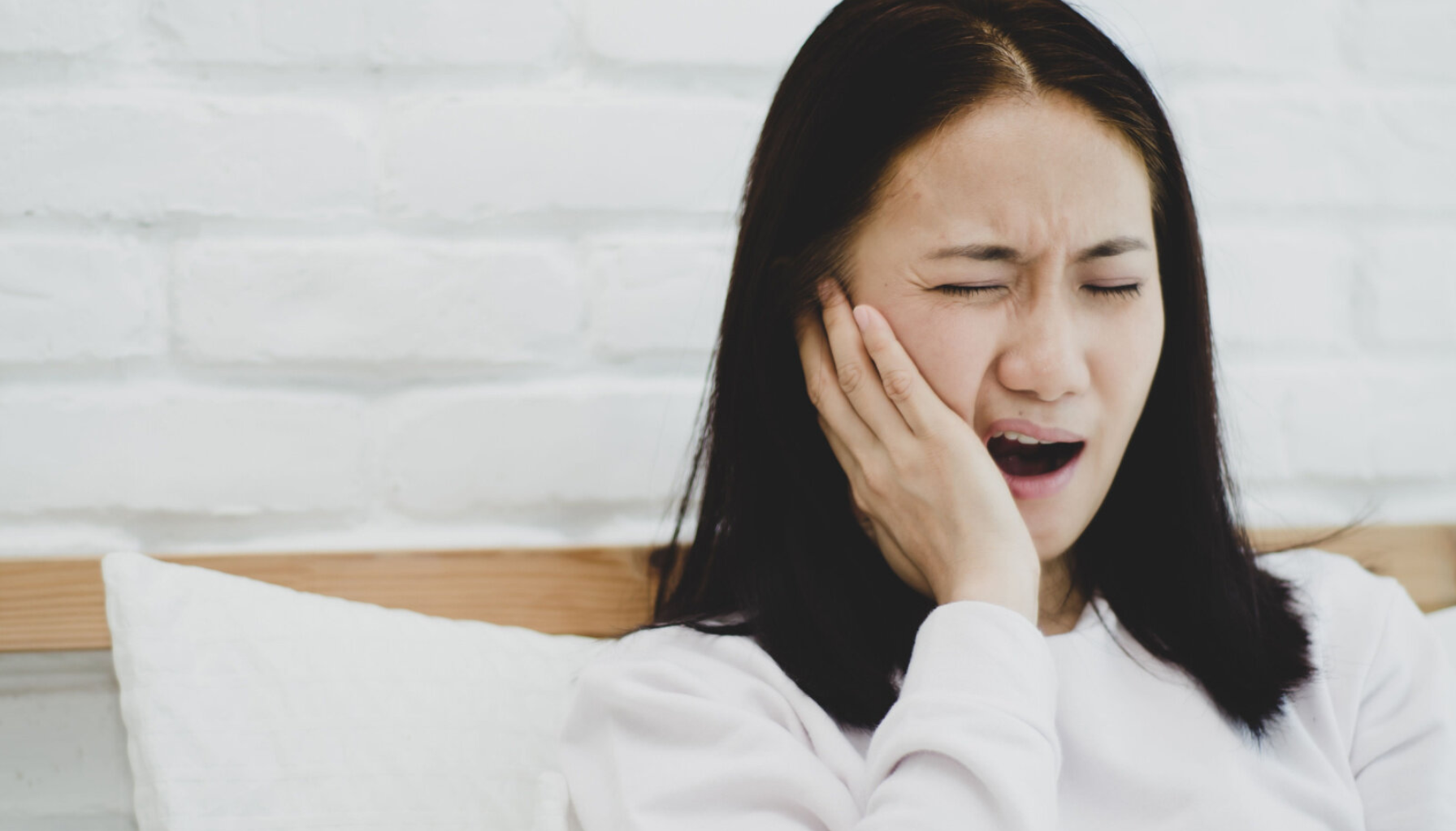 Vondt i Tann Når Jeg Biter Sammen? Ikke Ignorer Det! 11 Kvinne med lukkede øyne og åpen munn holder seg til kinnet i smerte – mulig tannverk eller kjeveproblem tidlig om morgenen. tennene dine tannpine munnen ulike bakterier