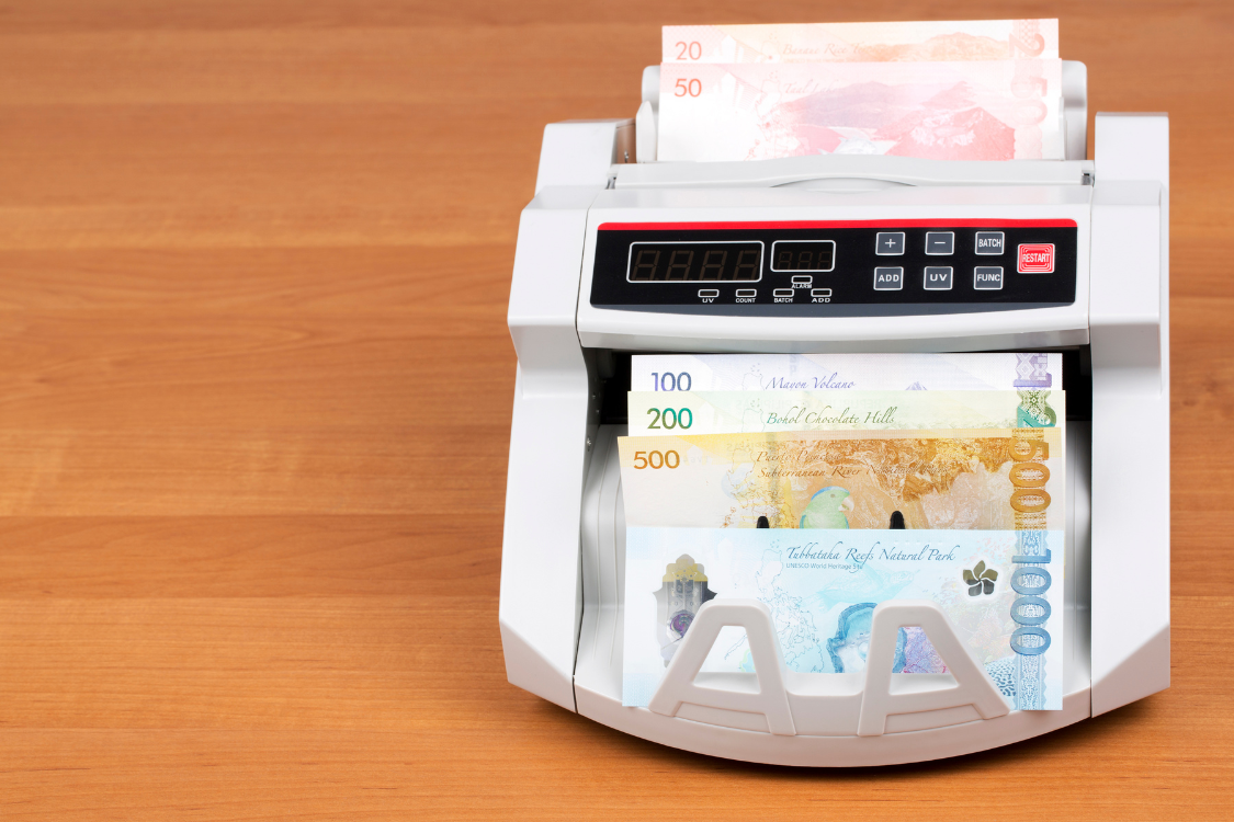 Currency counting machine processing Philippine bills, reflecting payroll and compensation calculations