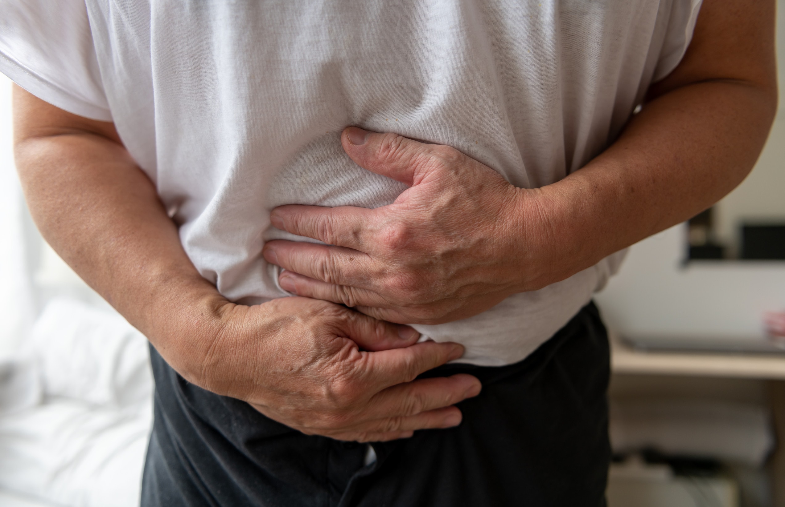 A man in a white t-shirt holds his stomach in pain after suffering bacterial food poisoning