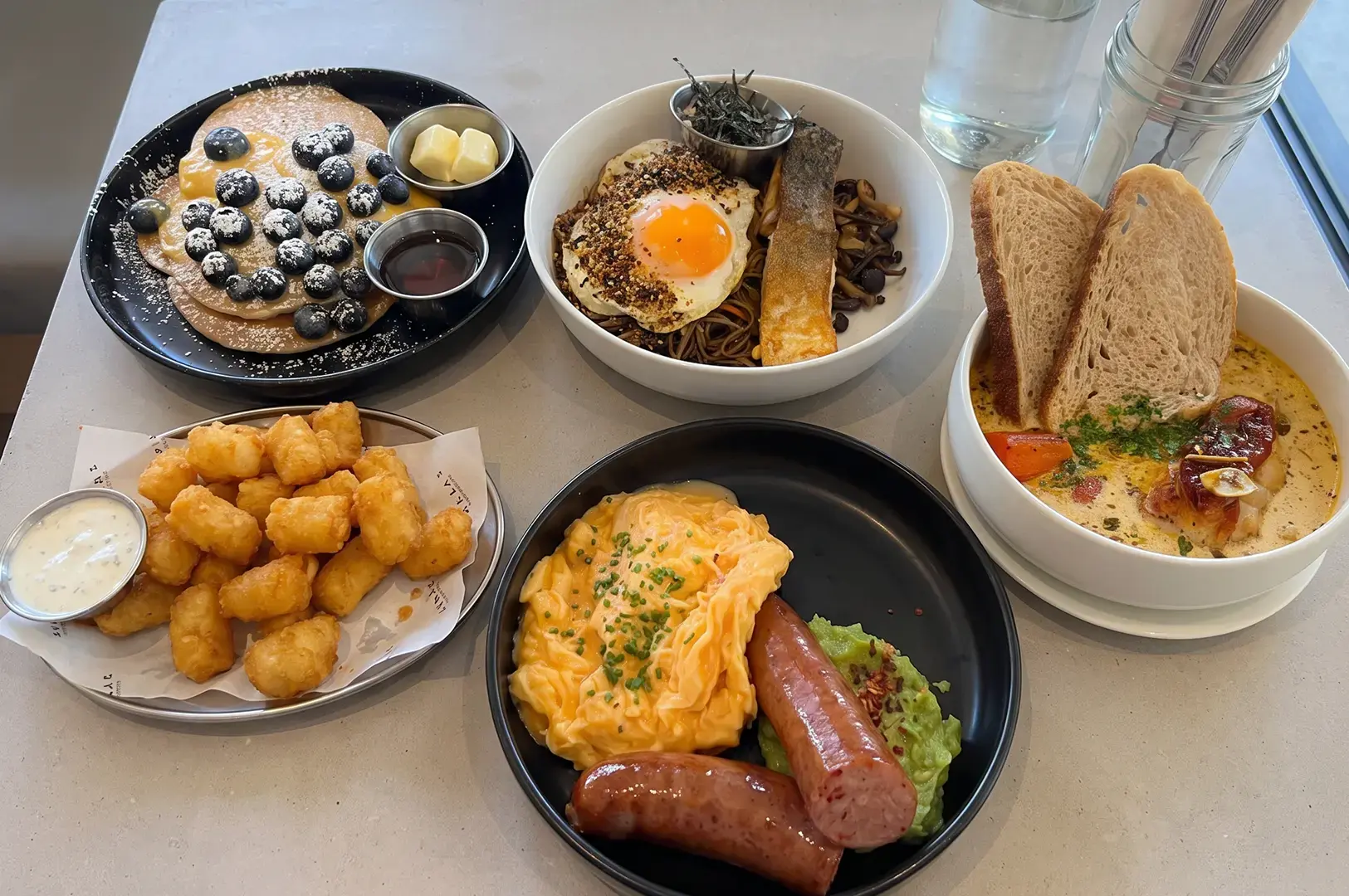 Atlas Coffeehouse signature menu items arranged on a white table, including Hotcakes & Passionfruit Curd. Wurst Rosti, and more.