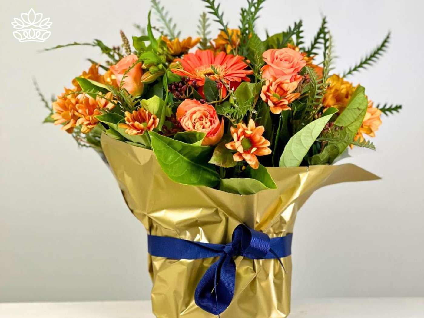An arrangement of orange flowers wrapped in gold paper and tied with a blue ribbon. Fabulous Flowers and Gifts. Gifts for Him. Delivered with Heart