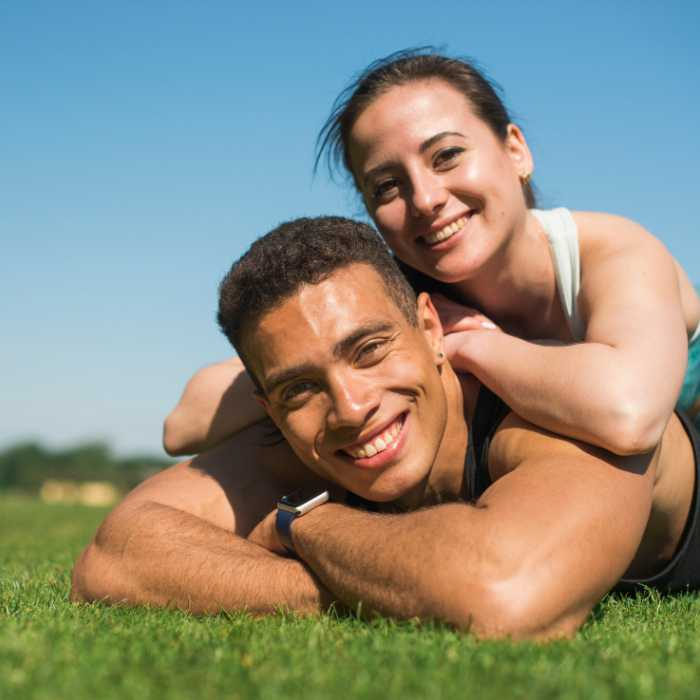A joyful couple relaxing on a sunny grass field, showcasing the happiness and health associated with the AIM Companies Supplements Collection. The couple embodies a lifestyle free from issues like constipation, a benefit highlighted on The Good Stuff Health Shop South Africa's website, where customers can create accounts and find directions for product use.
