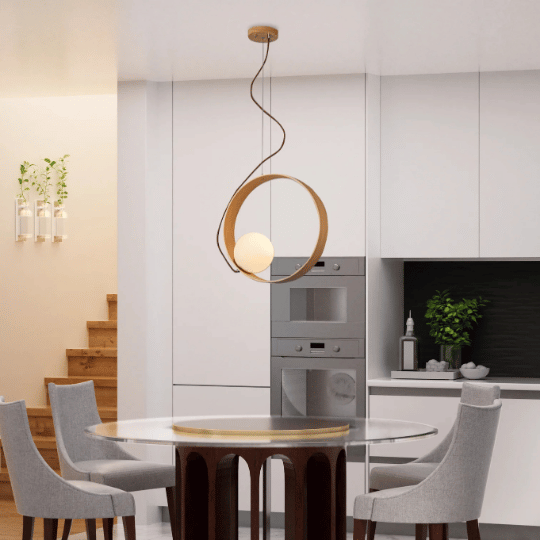 Japandi-style pendant light with a wooden circular frame surrounding a soft glowing orb, suspended above a modern dining table in a sleek, minimalist kitchen with white cabinetry.