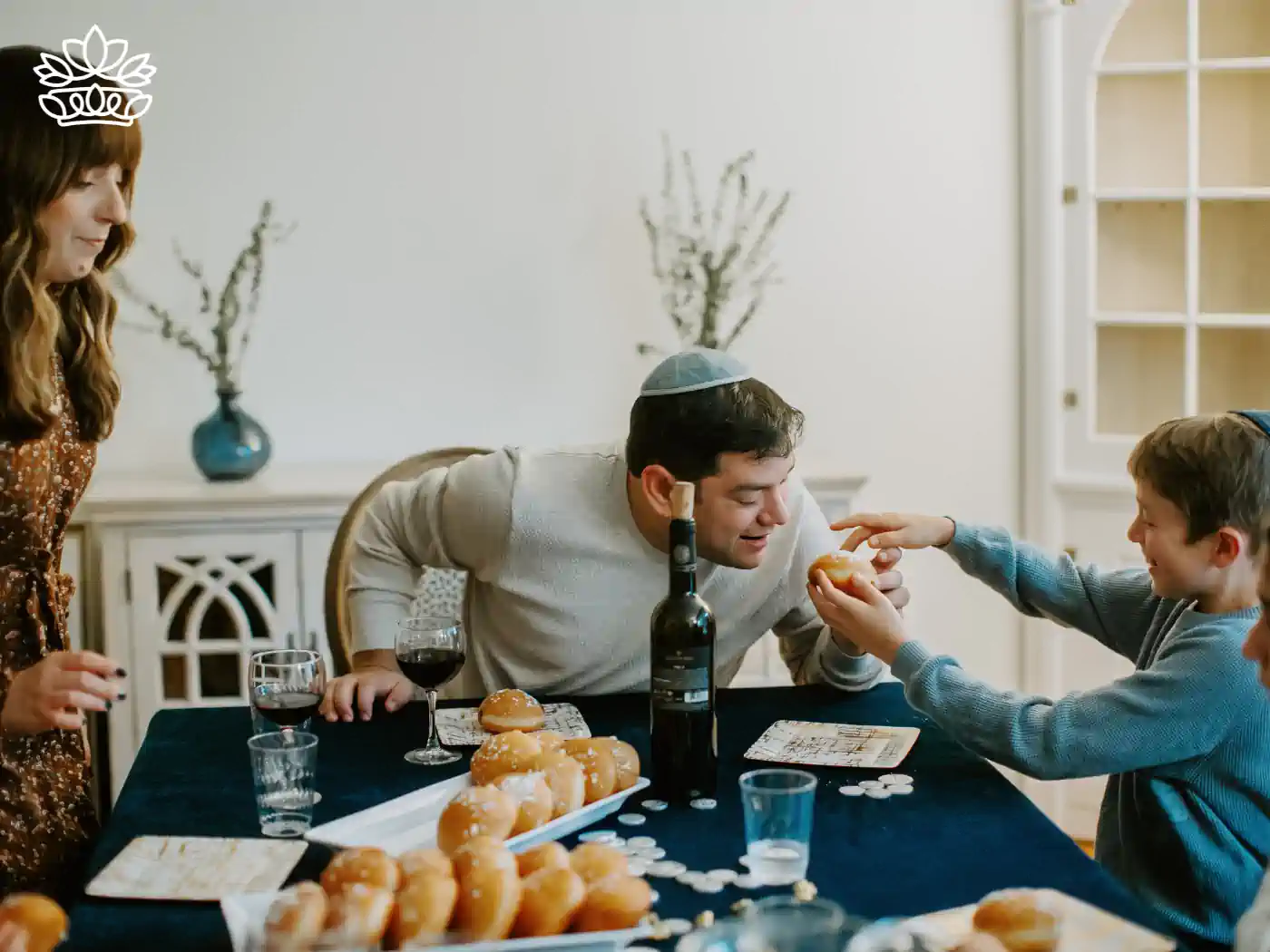 A family enjoying a meal together, with a boy offering a doughnut to a man, symbolizing Hanukkah traditions. Fabulous Flowers and Gifts - Hanukkah Collection.