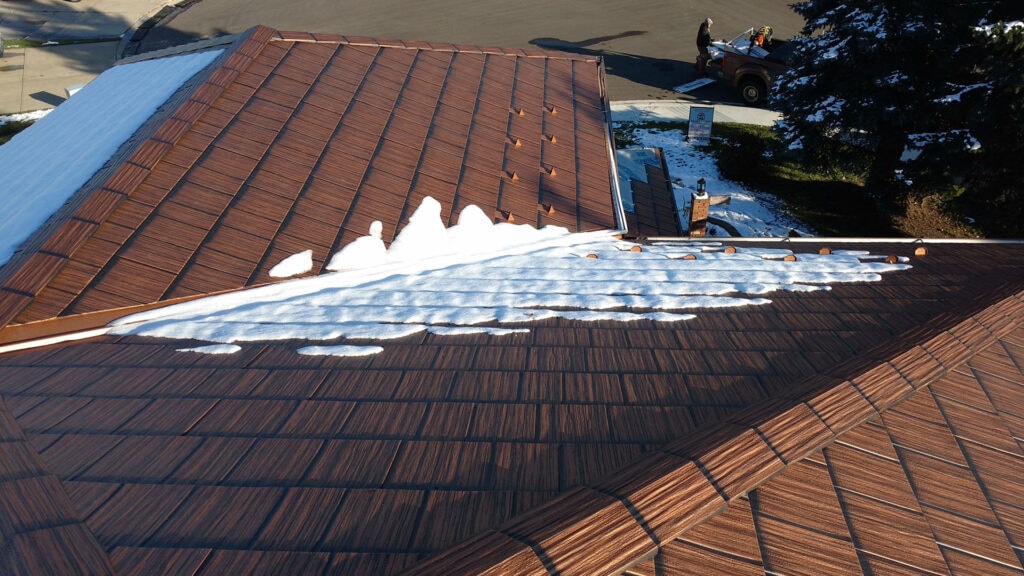 A picture of a metal roof in the winter. There is snow on the roof and on the ground.