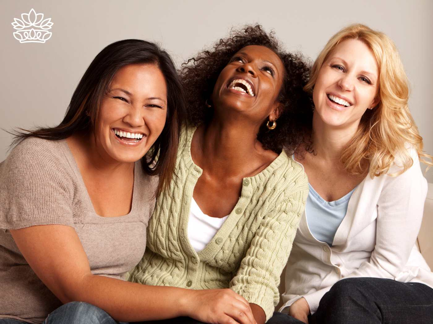 Three women of diverse backgrounds laughing together, exemplifying joy and friendship. Perfect for finding a good gift for Mother's Day, such as gift hampers that may include specialty bars from the Gifts Boxes for Women Collection. Fabulous Flowers and Gifts.
