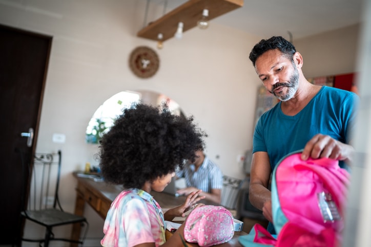 Dad putting items in his daughter's backpack.