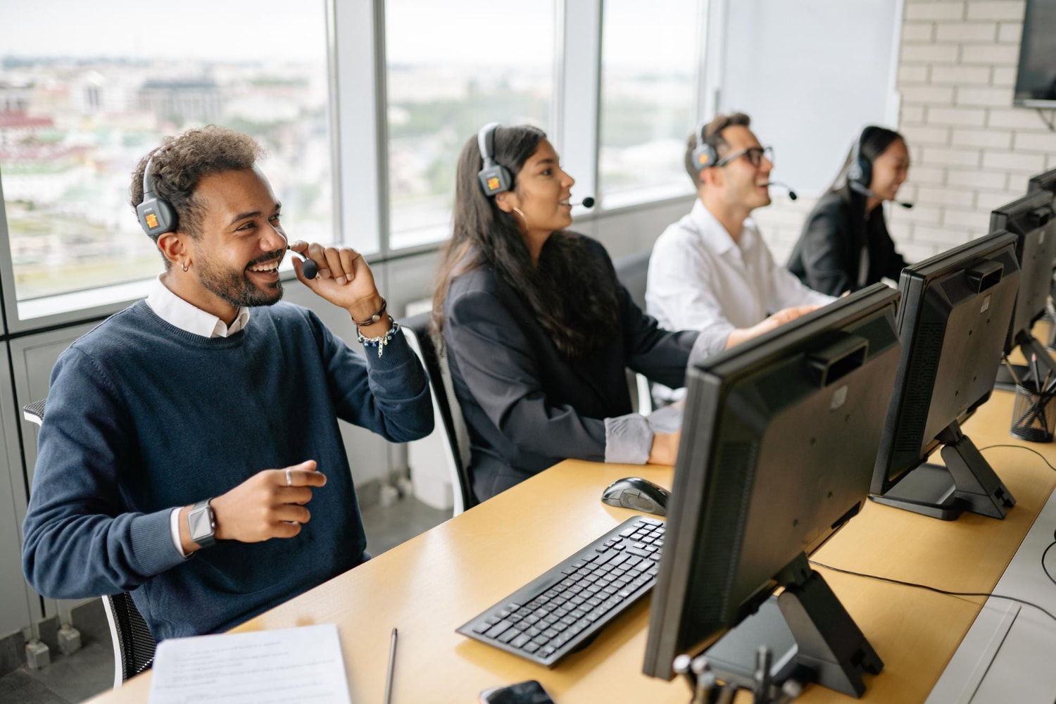 A team of agents sits at their desks, actively responding to customers via voice calls and digital channels. The modern office setting, with large windows, emphasizes the use of scalable contact center platforms for seamless customer support.