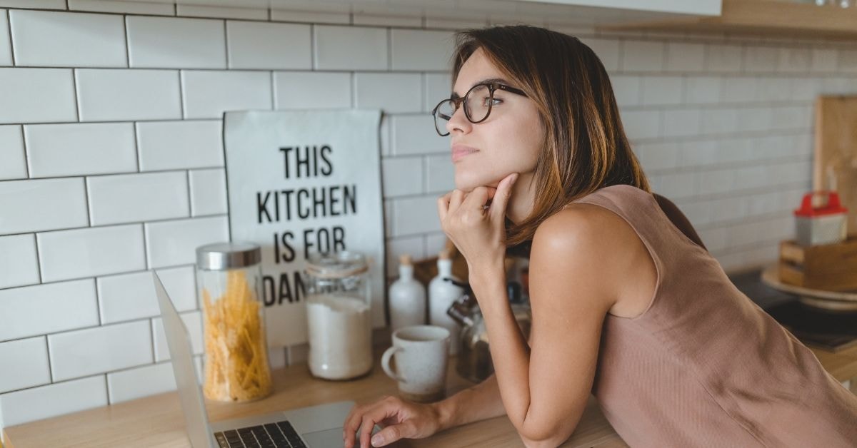 Woman in a kitchen, thoughtfully considering her OnlyFans LLC tax estimator results on a laptop.