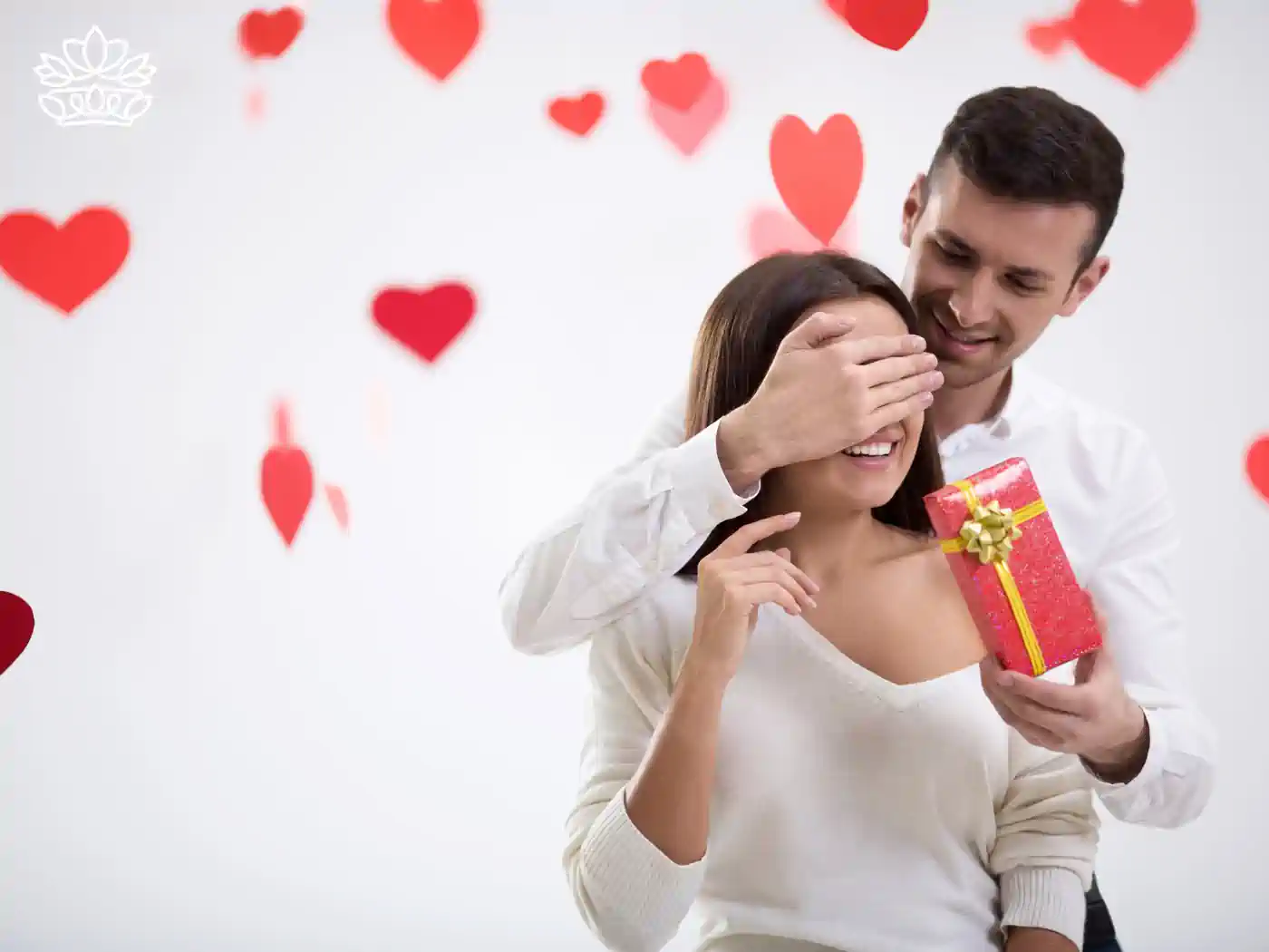 A man surprising a woman with a red gift box, surrounded by floating red hearts, highlighting the joy of gift-giving. Fabulous Flowers and Gifts. Romantic Gift Boxes.
