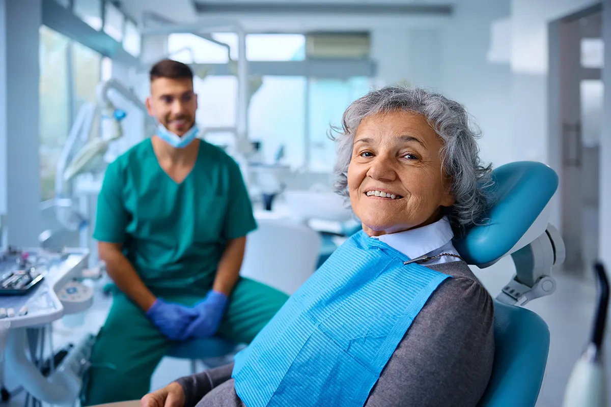 Smiling elderly patient in dental chair with practitioner in background