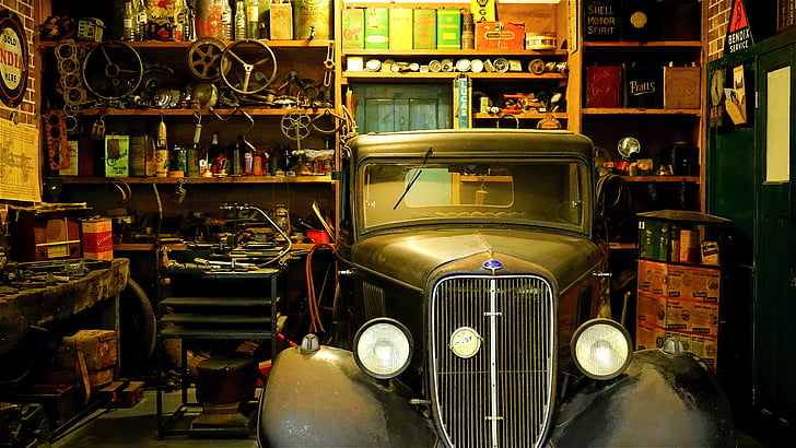 A classic car in a garage with tools and parts around it, being prepared for sale.